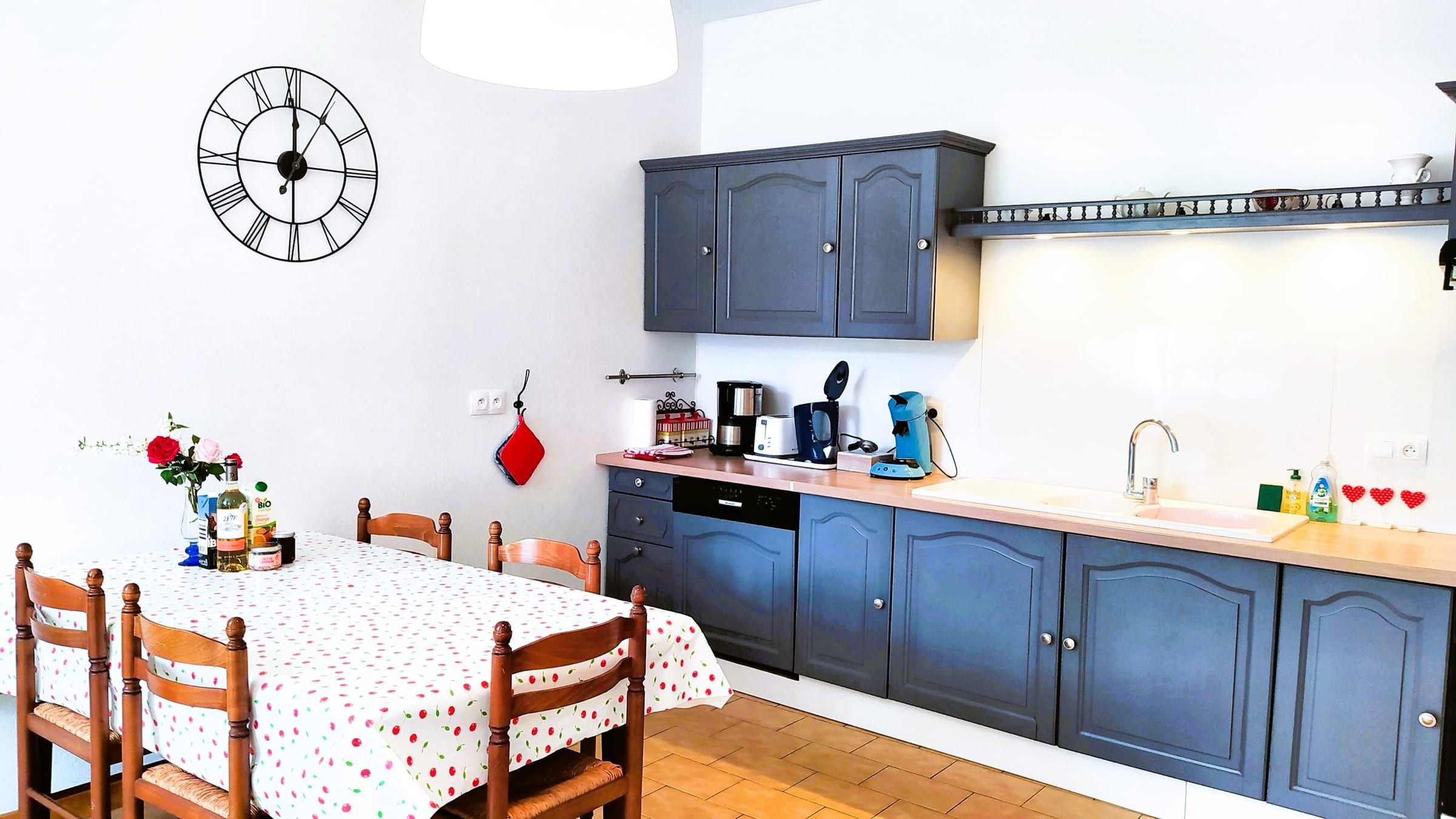 Cuisine moderne équipée aux placards gris, avec table et nappe fleurie