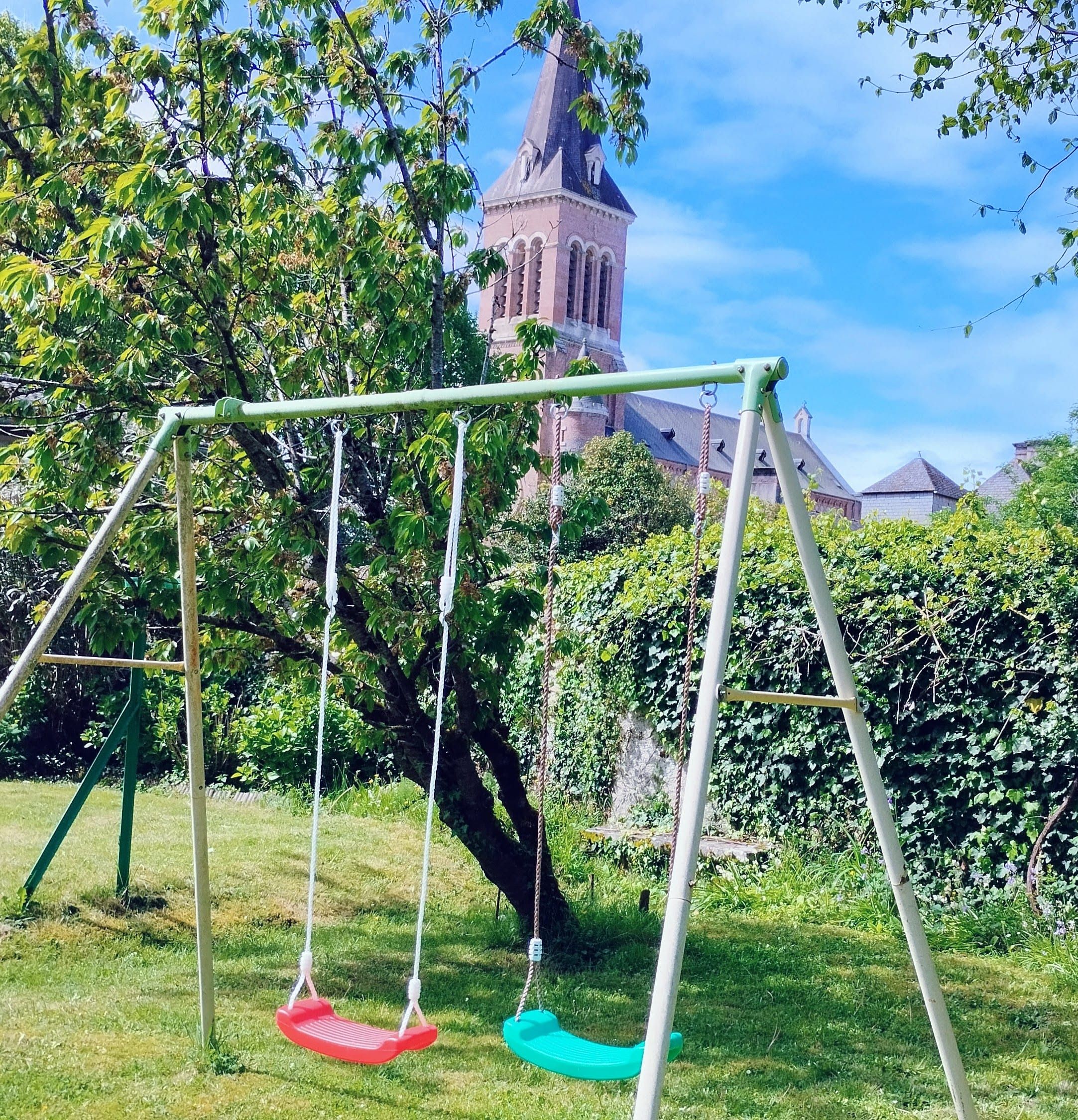 Balançoire dans le jardin clos, clocher du village en fond