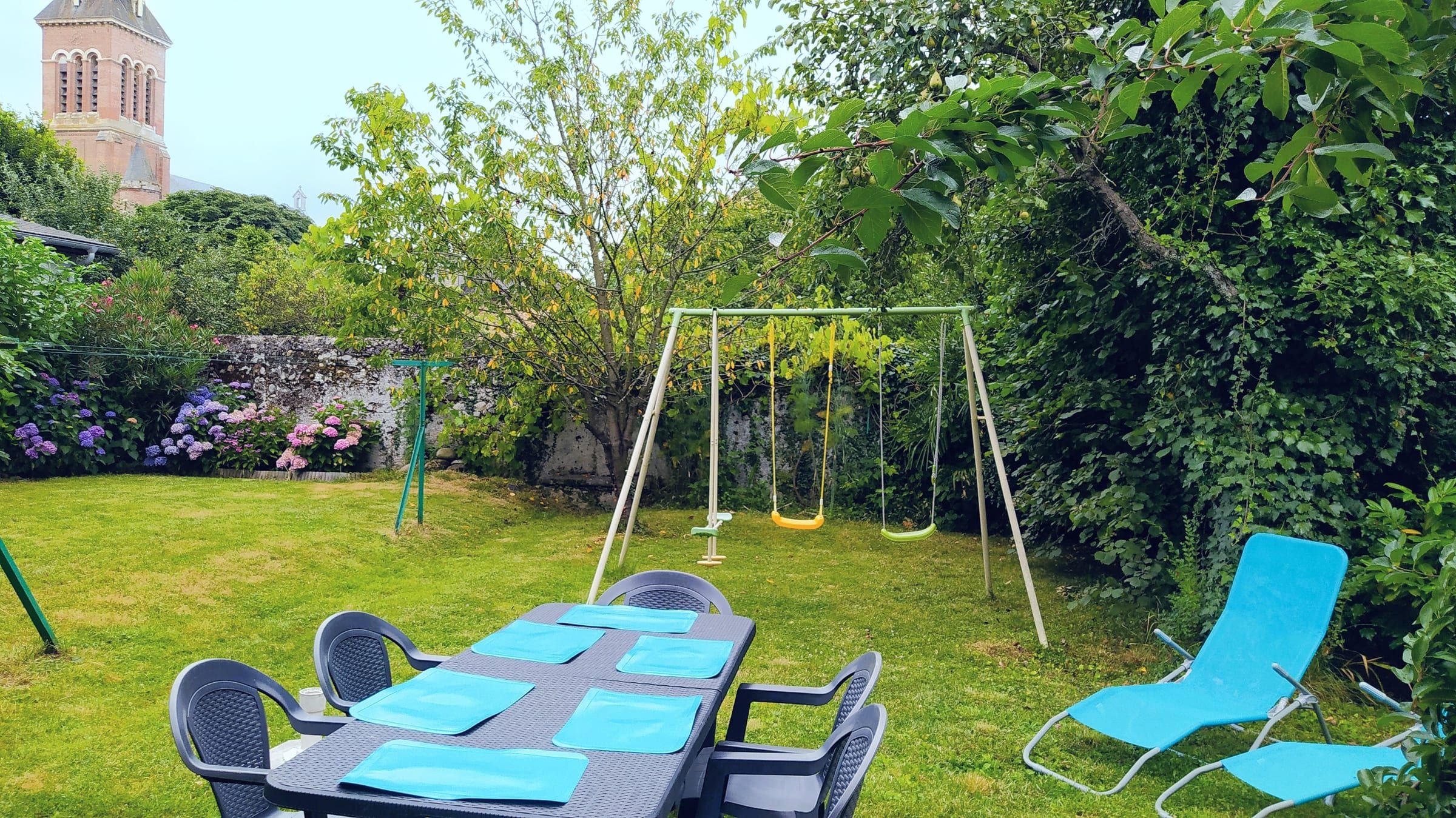 Jardin clos avec grande table, balançoire et pelouse verte au printemps