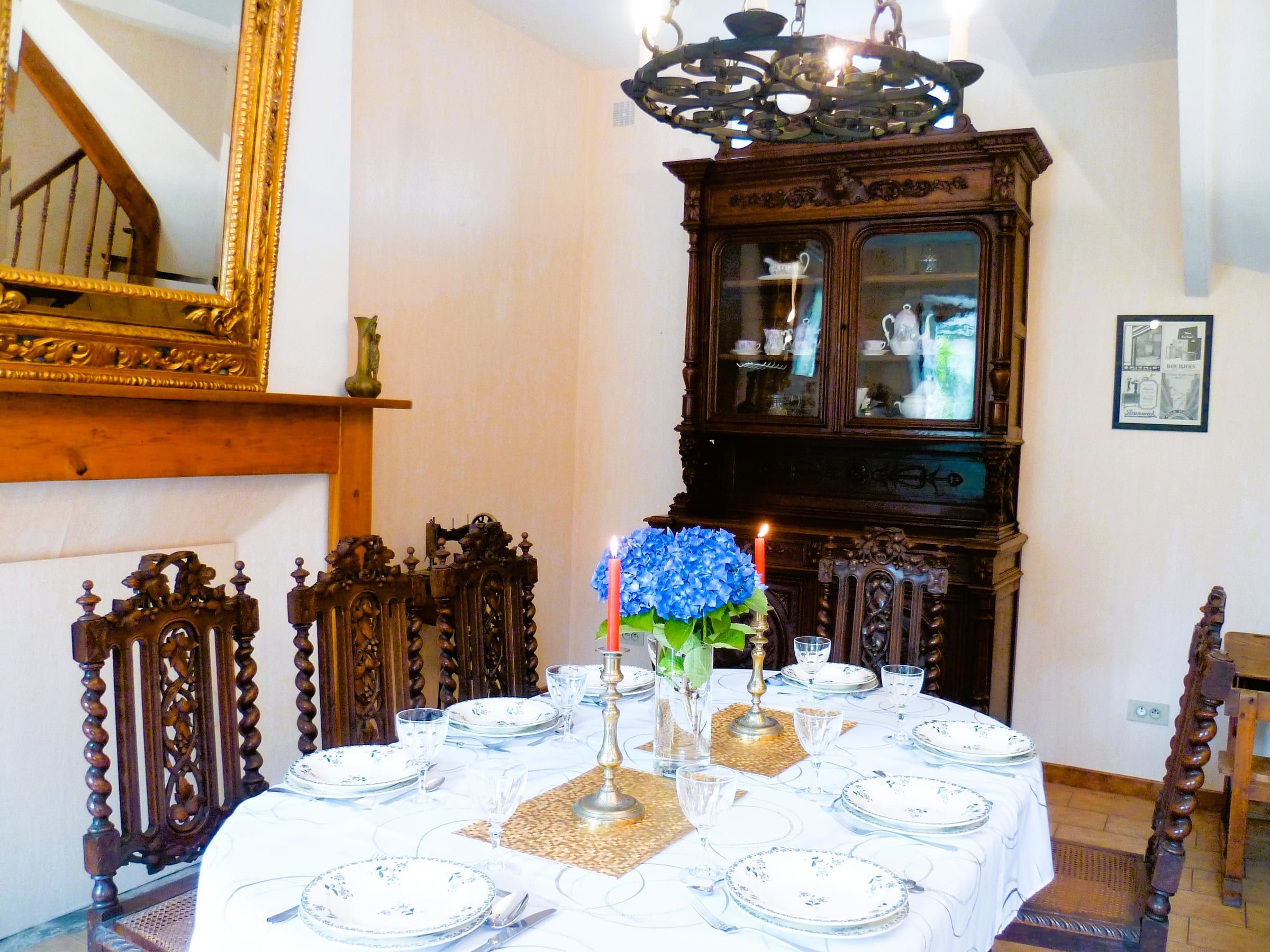 Salle à manger avec grande table dressée, chaises sculptées et vaisselier ancien
